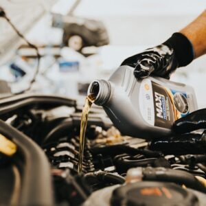 Close-up of a mechanic pouring engine oil into a car engine in an auto repair shop.