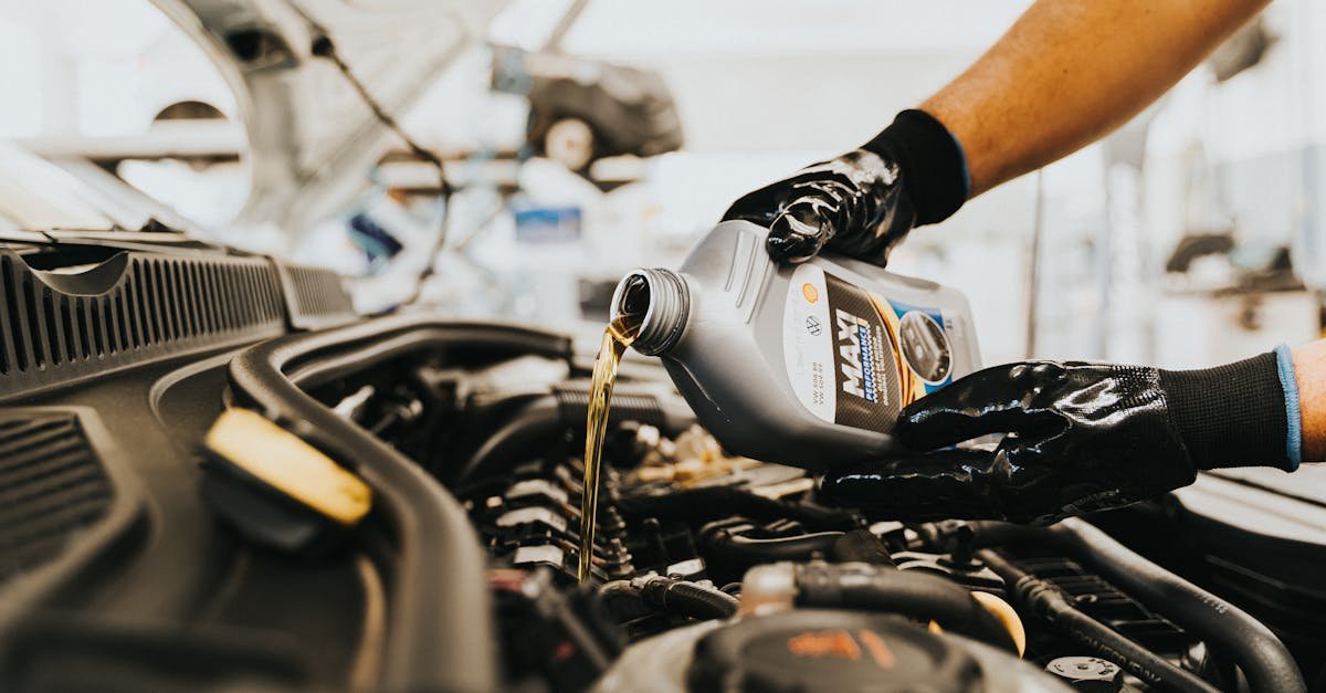 Close-up of a mechanic pouring engine oil into a car engine in an auto repair shop.
