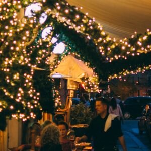 Inviting street view of a Trattoria Pizzeria with twinkling lights on a lively night.