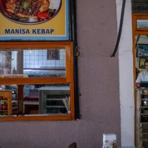 Cozy indoor view of a Turkish restaurant with Manisa kebab posters and a waiter at the counter.