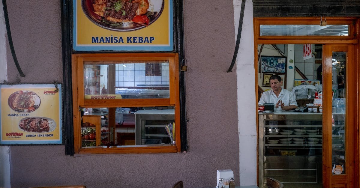Cozy indoor view of a Turkish restaurant with Manisa kebab posters and a waiter at the counter.