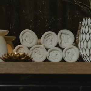 Serene spa setting featuring rolled towels, candlelight, and decorative vases on a wooden shelf.