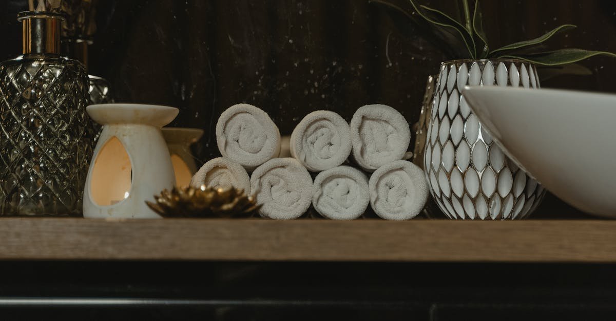 Serene spa setting featuring rolled towels, candlelight, and decorative vases on a wooden shelf.